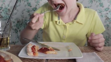 Restoranda pizza yiyen bir çocuk, büyük bir dilim pizza koyar ve çiğner.