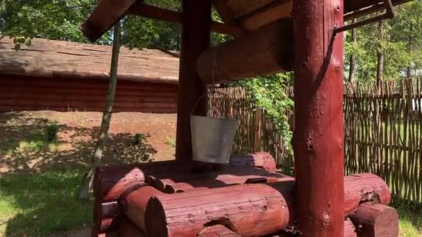 Un pozo de agua rústico de madera con un cubo en una cuerda en una granja en el día soleado de verano — Vídeos de Stock