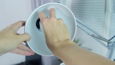 Kadın eli değişiyor, ofiste kurşun bir ampulü değiştiriyor, ampulü lambanın tutacağına takıyor.