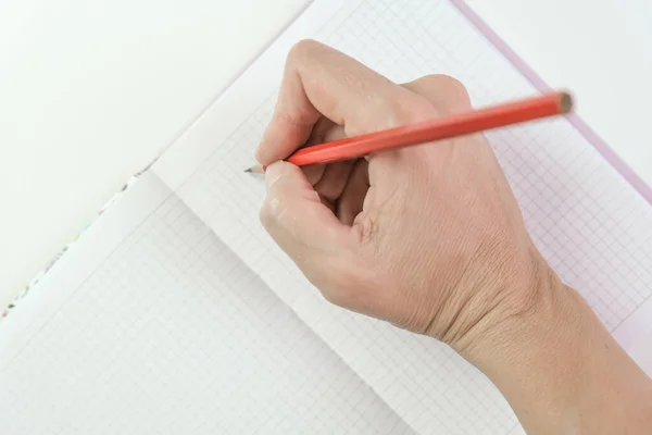 Female hands holding red pencil and writing something in a notebook, goal setting and planning concept.