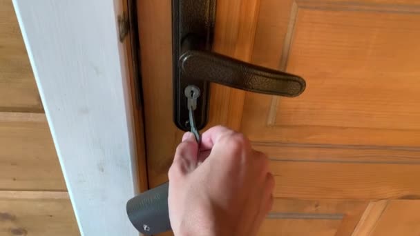 Sebuah tangan memegang kunci dan memasukkannya ke dalam lubang kunci, membuka dan membuka pintu kayu putih, keamanan rumah dan konsep perlindungan — Stok Video