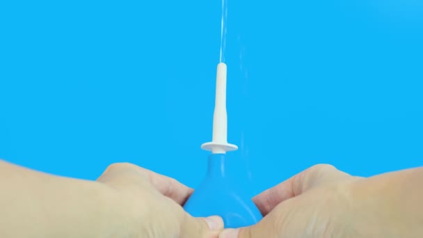 Hand met een blauwe klysma pompend, injecterend water op een blauwe achtergrond — Stockvideo