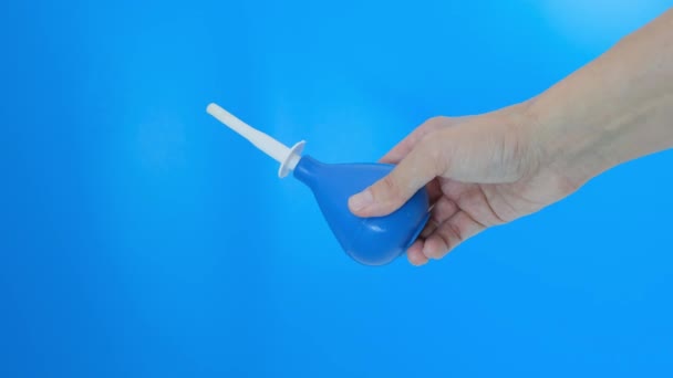 Hand met een blauwe klysma pompen, comprimeren, knijpen en injecteren van water op een blauwe achtergrond — Stockvideo