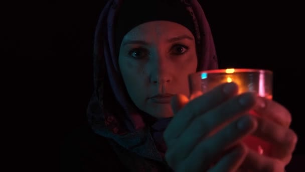 Ένα νυχτερινό πορτραίτο μιας μάγισσας που ρίχνει ξόρκι πάνω από ένα κόκκινο κερί και κάνει μαγεία, μετακινεί ένα κερί κοντά στην κάμερα και σβήνει μια φλόγα — Αρχείο Βίντεο