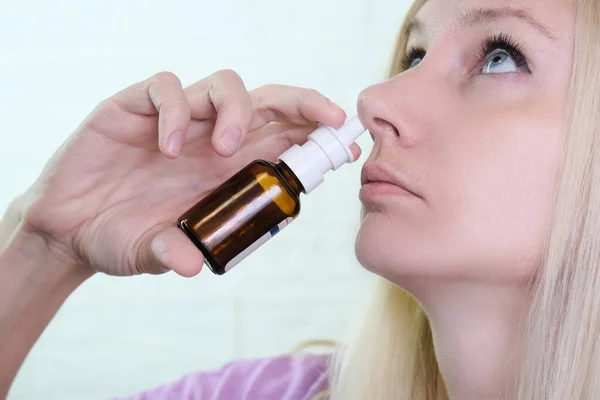 A woman with a runny nose holds a medicine in her hand, nasal spray irrigations to stop allergic rhinitis and sinusitis.