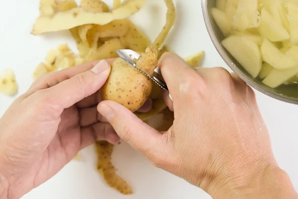 Hands of a woman housewife peeling raw potato with a special tool knife close up, top view.