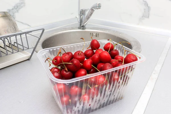 Ripe sweet cherry close upon a kitchen table, cleaning fresh juicy fruits in plastic containers of bacteria and dirt, tasty summer berries.