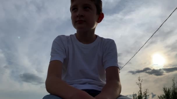 A lonely sad boy sitting outdoors on a bench at sunset, unhappy depressed child with discrimination and bullying problems — Stock Video