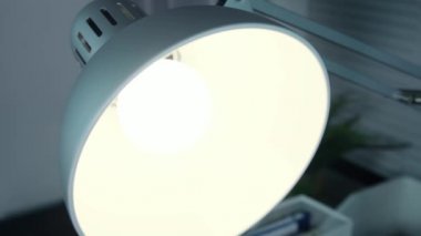 Kadın elleri ışığı kapatıyor ve sonra kaldırıyor, değiştiriyor, ofisteki kurşun ampulü değiştiriyor, ampulü takıyor, lambayı tutacağına takıyor.