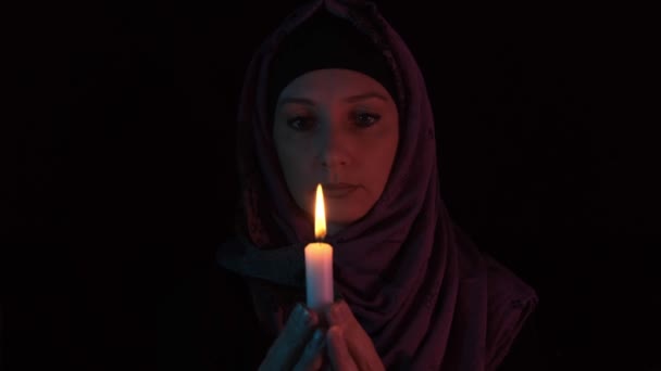 Egy nő egy fejkendőben, égő gyertyával a kezében, imádkozva Istenhez a sötétségben, a gyertya rejtélyesen elaludt. — Stock videók