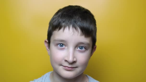 En leende pojke som gör roliga ansikten och grimaser nära mot gul bakgrund — Stockvideo