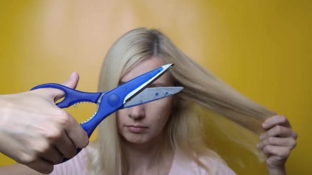 Gros ciseaux cliquetant devant une femme blonde aux cheveux longs, concept de coupe de cheveux sur fond jaune — Video