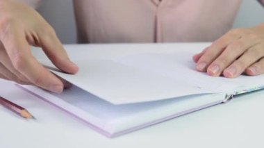 Masanın yanında elinde kalem, defter ve parmaklarıyla oturan bir kadın gergin ve bir yaprak çıkarıp buruşturuyor.