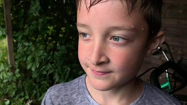 Un retrato de un niño con gotas de lluvia en la cara y cabello mojado después del aguacero, mal tiempo y tormenta en verano — Foto de Stock