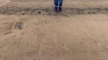 Üzgün, düşünceli bir çocuk bir göl kıyısında duruyor ve önüne bakıyor, soğuk bir yaz günü ve kasvetli bir hava