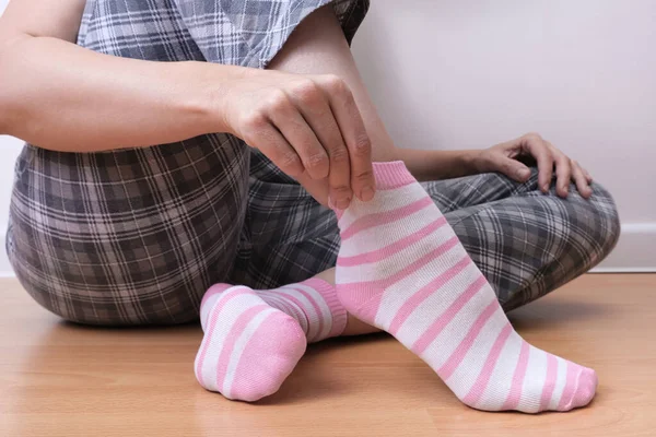 A woman sitting on the floor and putting on pink and white striped cozy cotton socks on her feet, warming legs and body in autumn and winter