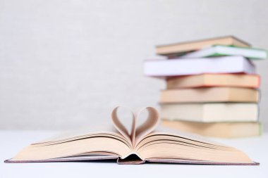 Kitap sevgisi, okuma, masanın üzerinde duran bir yığın kitap ve önünde kalp şeklinde kıvrımlı yapraklar olan açık kitap, uzayı kopyalamak.