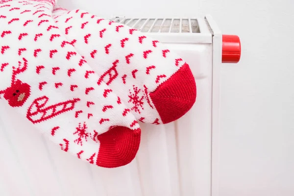 White and red christmas socks hanging on warm central heat radiator, winter holiday home mood