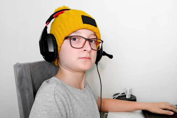 Een gamer jongen in een trendy gebreide muts en heaphones zitten aan de tafel en spelen multiplayer computerspel op laptop — Stockfoto