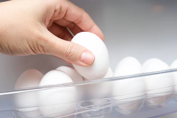 A hand taking white hen chicken egg from a shelf of a fridge, protein source for health, ingredients for fast breakfast for dieting, slimming and sports person — Stock Photo, Image