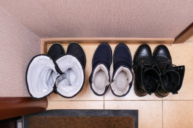 Evin girişinde yerde üç çift sıradan kış ayakkabısı koridorda aile ayakkabısı.