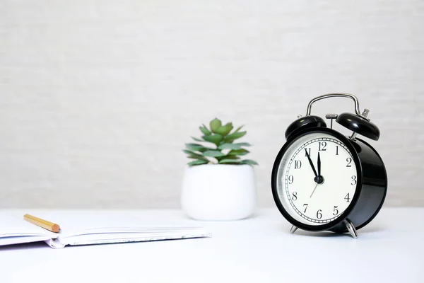 Relógio despertador mostrando 5 minutos a doze e um notebook com um lápis amarelo como um conceito de prazo de relatório de imposto de negócios com espaço de cópia — Fotografia de Stock