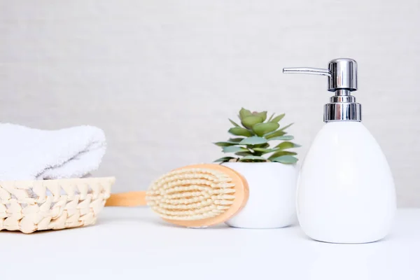 Fehér kerámia szappan adagoló, spa törölköző, növényi és masszázs kefe fehér asztal belsejében fényes fürdőszoba háttér — Stock Fotó