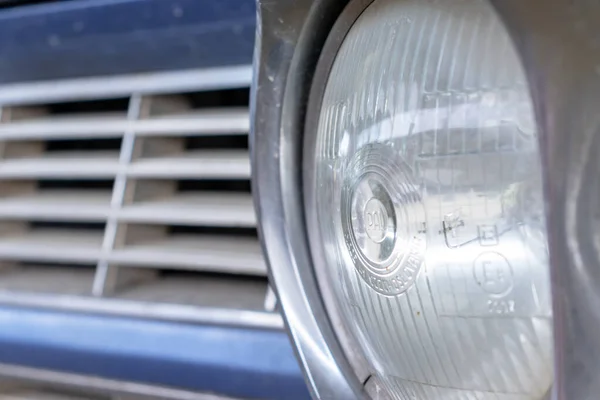 A headlight of a blue retro old car close up in a junk yard, changeover from old to a new modern car — Stock Photo, Image