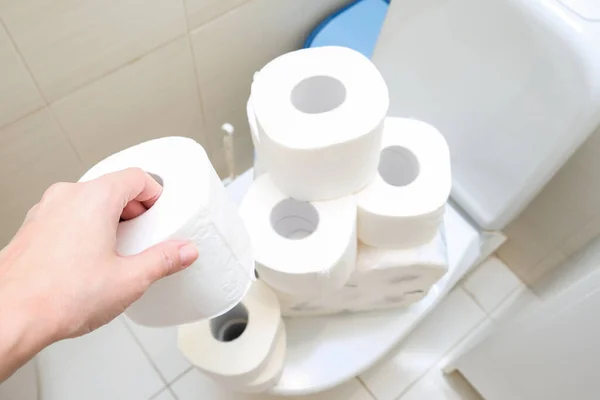 Molti rotoli di carta igienica a casa di accumulatore, l'acquisto di troppi mezzi igienici durante la pandemia, una mano che tiene un rotolo di carta igienica in un bagno — Foto Stock