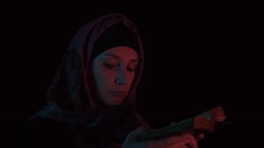 Türbanlı bir kadın gecenin karanlığında eski bir İncil 'i açıp Tanrı' ya dua ediyor.