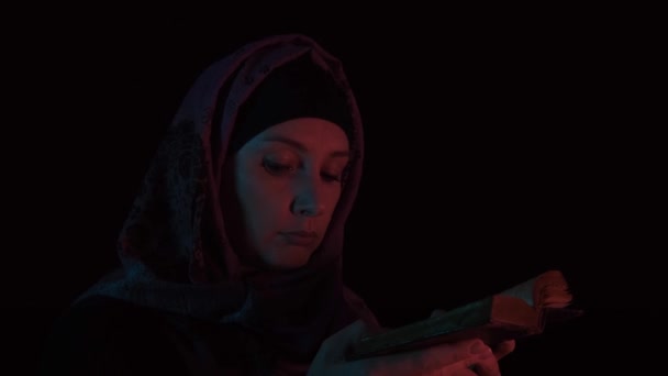 Жінка в головному уборі відкриває стару Святу Біблію в темряві вночі і молиться Богу — стокове відео