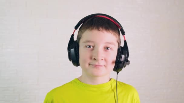 Um retrato de um menino caucasiano em fones de ouvido modernos de perto, ele está sorrindo e olhando para a câmera — Vídeo de Stock