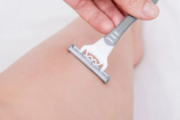 Frau rasiert Beine mit einem grauen Einweg-Rasiermesser aus Kunststoff in Nahaufnahme, unerwünschte Haare entfernen — Stockfoto