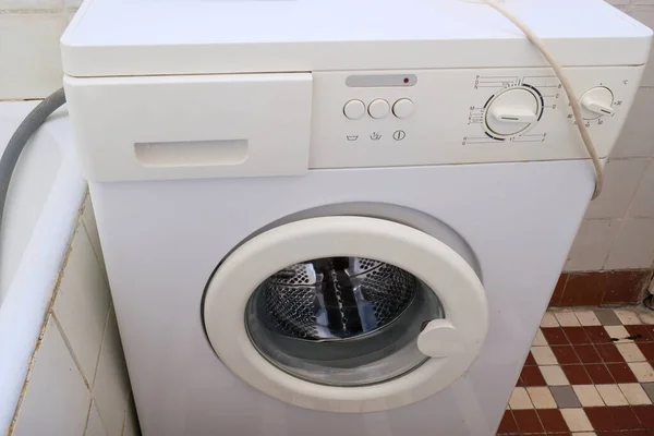 An old broken washing machine in a bathroom need to be recycled and replaced.