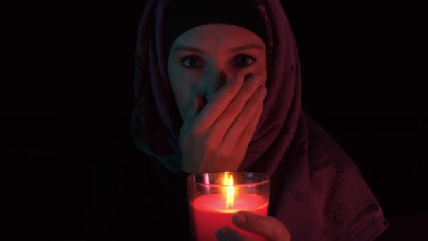 Una mujer afligida sosteniendo una vela roja encendida y cubriéndose la boca con palma — Vídeo de stock
