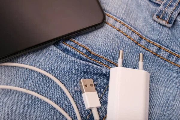 Charging smartphone concept, a usb cable for charging devices, gadgets with adapter plug and a phone on a jeans background