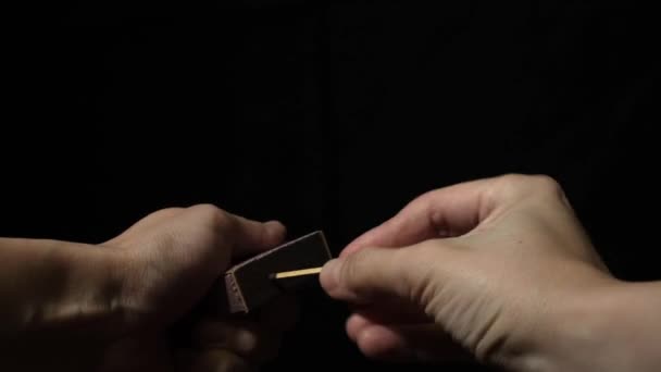 Hands lighting match in the dark, hold burning matchstick and a match box against black background — Stock Video