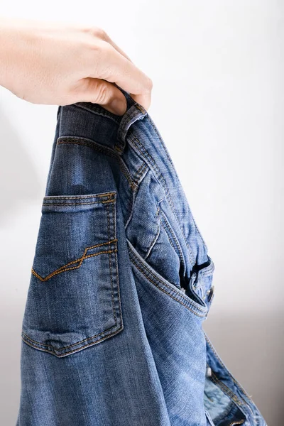 A hand holding used bluejeans on white background, recycling and reusing of worn clothes — Stock Photo, Image