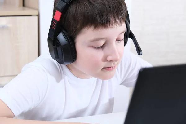 Um menino homeschooler com fones de ouvido sentado em um laptop e aprendizagem, conceito de educação on-line — Fotografia de Stock