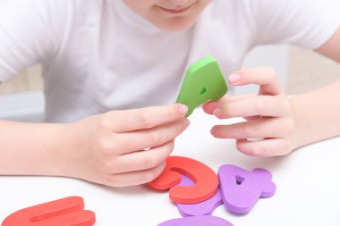 Harfleri ve alfabeyi öğrenen bir çocuk bir masada oturuyor ve ellerinde renkli köpük harfleri tutuyor.