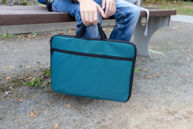 Bir okul çocuğu parkta oturuyor ve elinde ders kitaplarıyla ek eğitim dersinin başlamasını bekliyor.