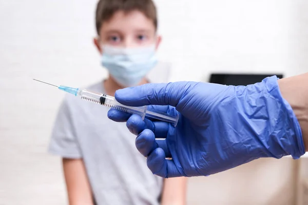 Ένας γιατρός ή νοσοκόμα με μια σύριγγα στο χέρι πρόκειται να εμβολιάσει ένα παιδί αγόρι — Φωτογραφία Αρχείου
