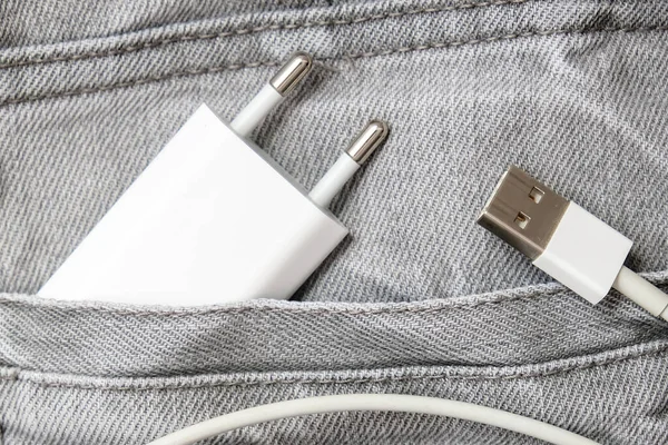 Cargador USB, enchufe de cable y adaptador en bolsillo gris vaqueros, no se olvide del cargador en casa — Foto de Stock