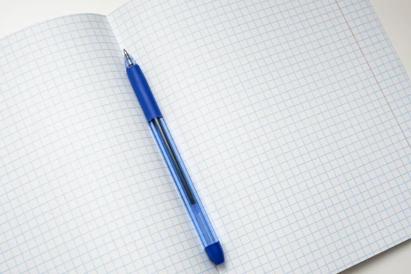 Un bolígrafo azul acostado en una hoja de cuaderno de la escuela a cuadros en blanco, papel con espacio de copia —  Fotos de Stock