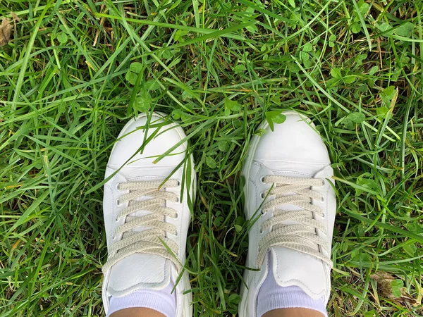 Samičí nohy v bílých kožených teniskách stojící na trávě v parku, koncept chůze — Stock fotografie