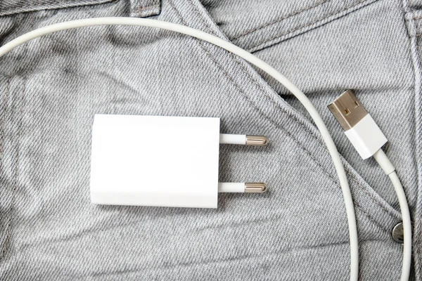 Cargador USB, enchufe de cable y adaptador en bolsillo gris vaqueros, no se olvide del cargador en casa — Foto de Stock