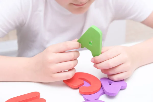 Dzieciak uczy się liter i alfabetu, siedzi przy stole i trzyma kolorowe piankowe litery w rękach — Zdjęcie stockowe