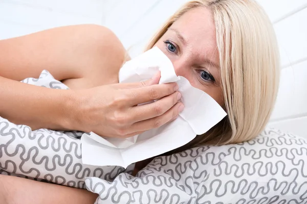 Joven europeo molesto y enfermo, que tiene la gripe femenina con servilleta de papel que sopla la nariz, se encuentra en la almohada. Tratamiento de la sinusitis. Rinitis, frío, enfermedad, concepto de alergia —  Fotos de Stock