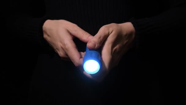 कैमरा, जासूस और जांच अवधारणा में नीले बीम के साथ अंधेरे में चमकते हुए एक एलईडी फ्लैशलाइट के साथ हाथ — स्टॉक वीडियो