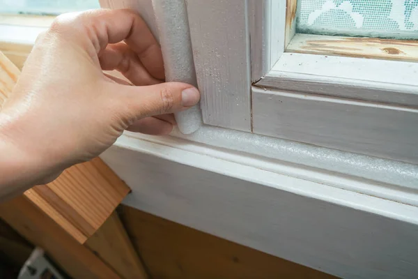 Kobieta ręcznie izoluje stare okna, aby zapobiec wyciekom ciepła i przeciągnięć, przygotowując dom na zimę i zimno — Zdjęcie stockowe